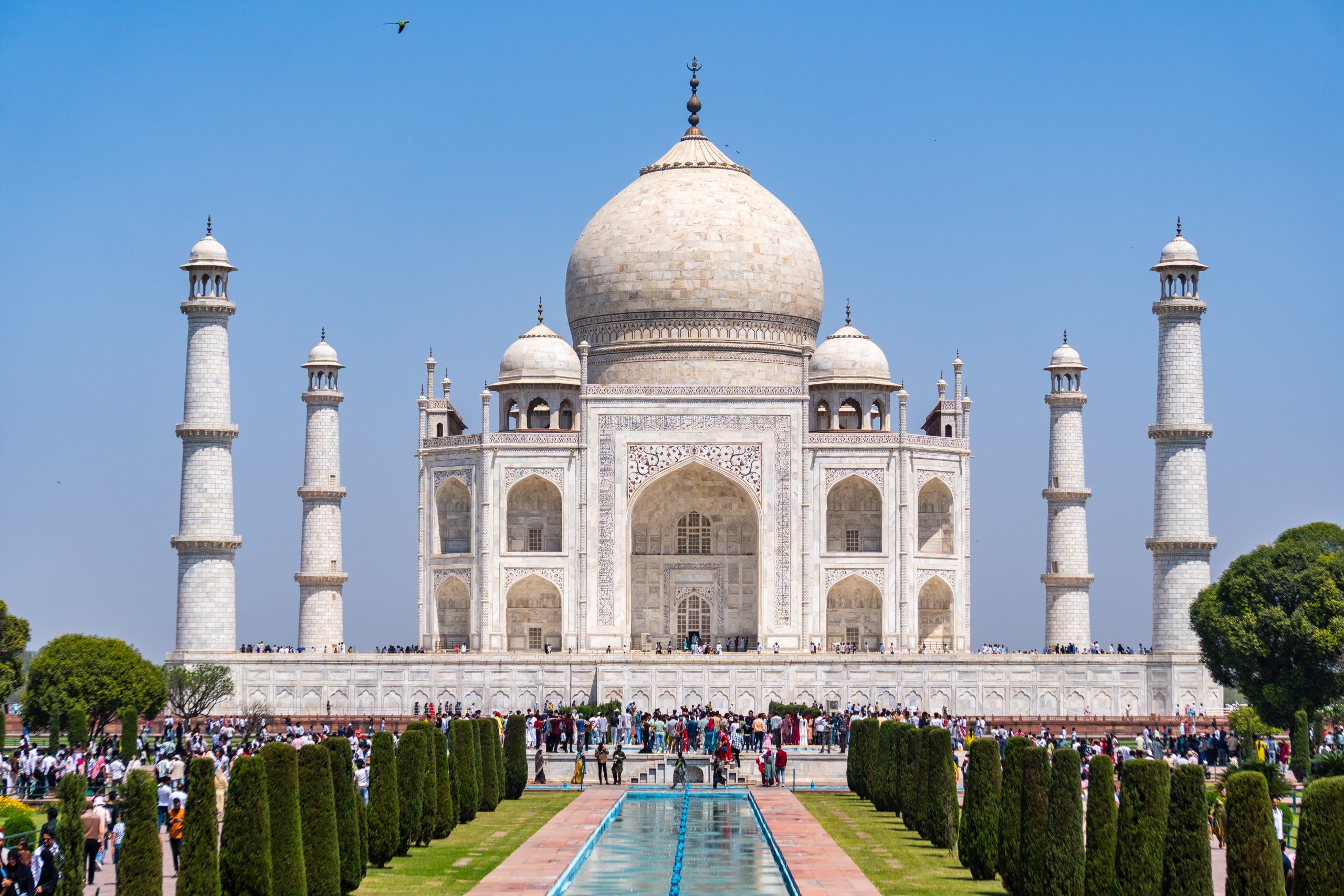 Front view of the Taj Mahal in daylight, showing its white marble facade, central dome, four minarets, and reflective pool